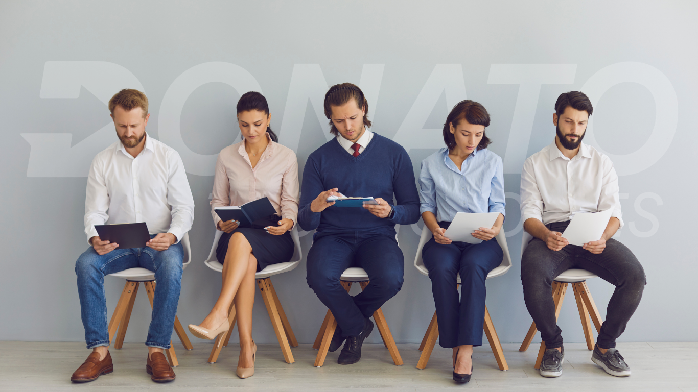 Five professionally dressed candidates sitting in a modern office lobby, waiting for job interviews.